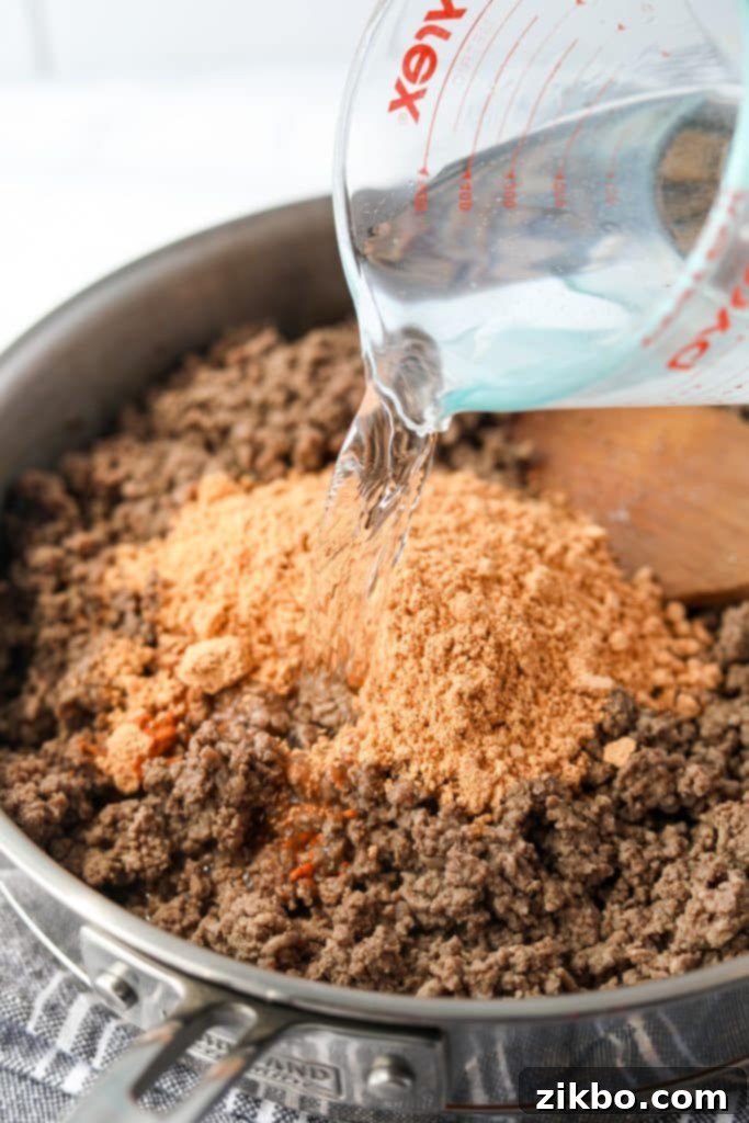Adding water and taco seasoning to the cooked ground meat in a skillet.