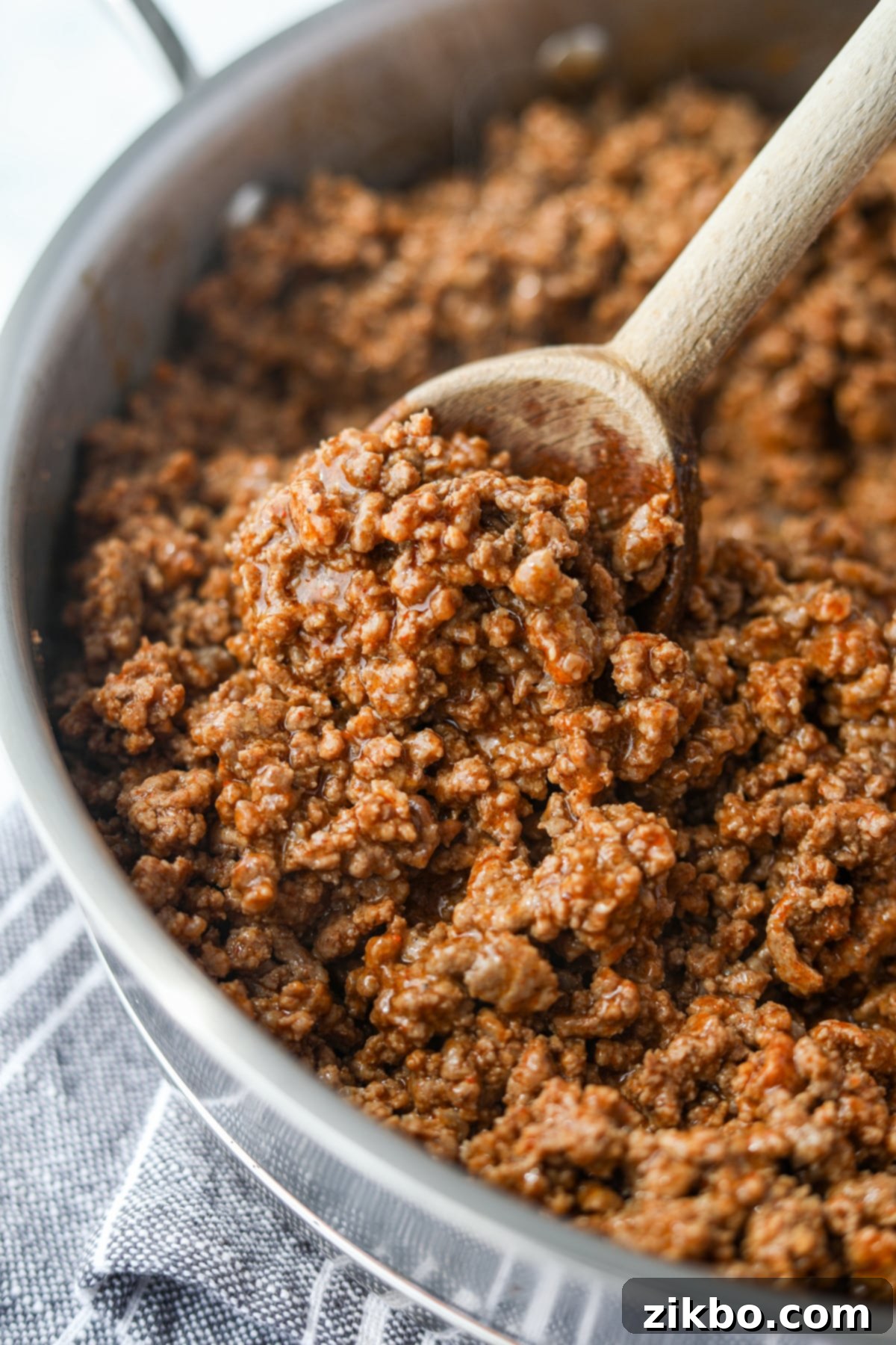 A skillet with ground beef being stirred by a wooden spoon, showcasing the rich texture.