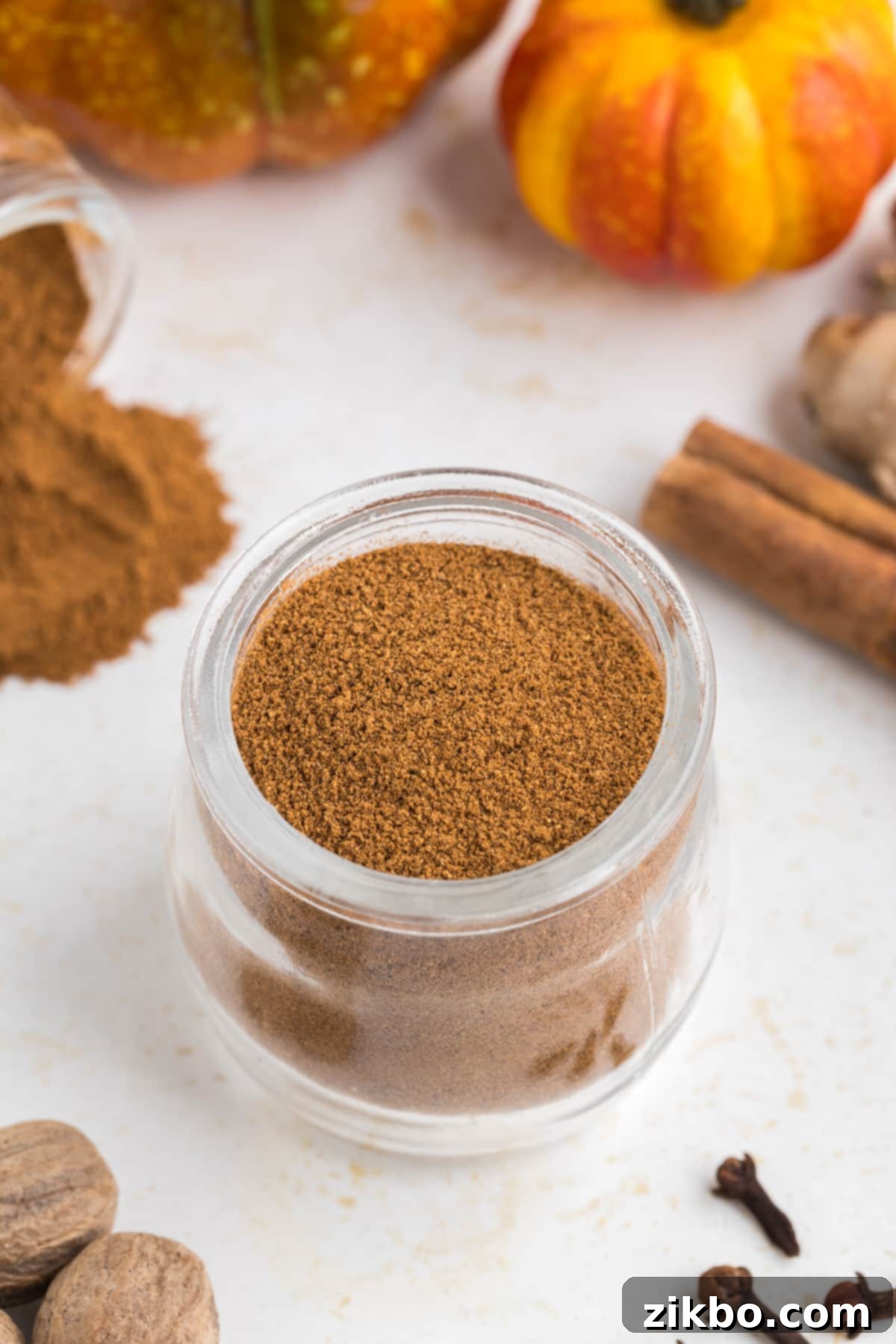 A small glass jar filled with homemade pumpkin spice, adorned with a decorative label, surrounded by whole spices and mini pumpkins.