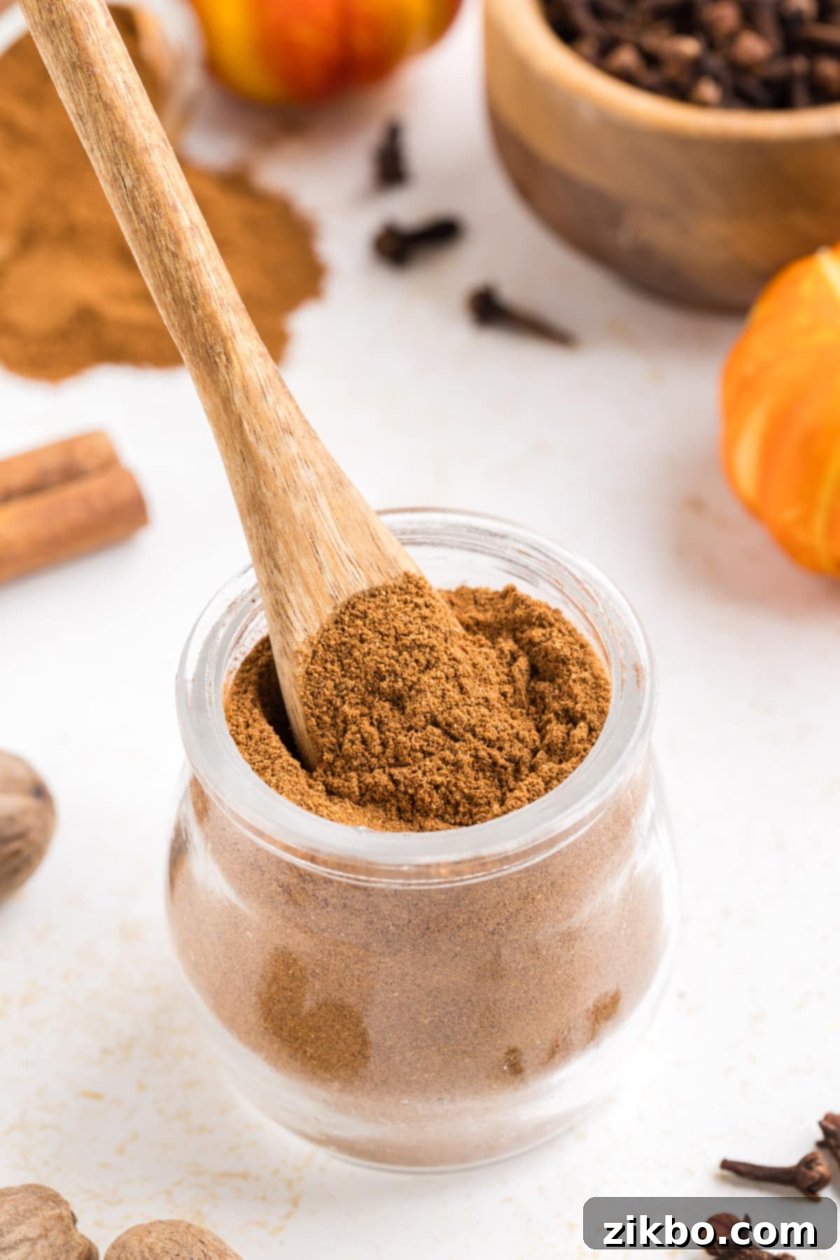 A small wooden spoon carefully taking a portion of pumpkin spice from a small glass jar.