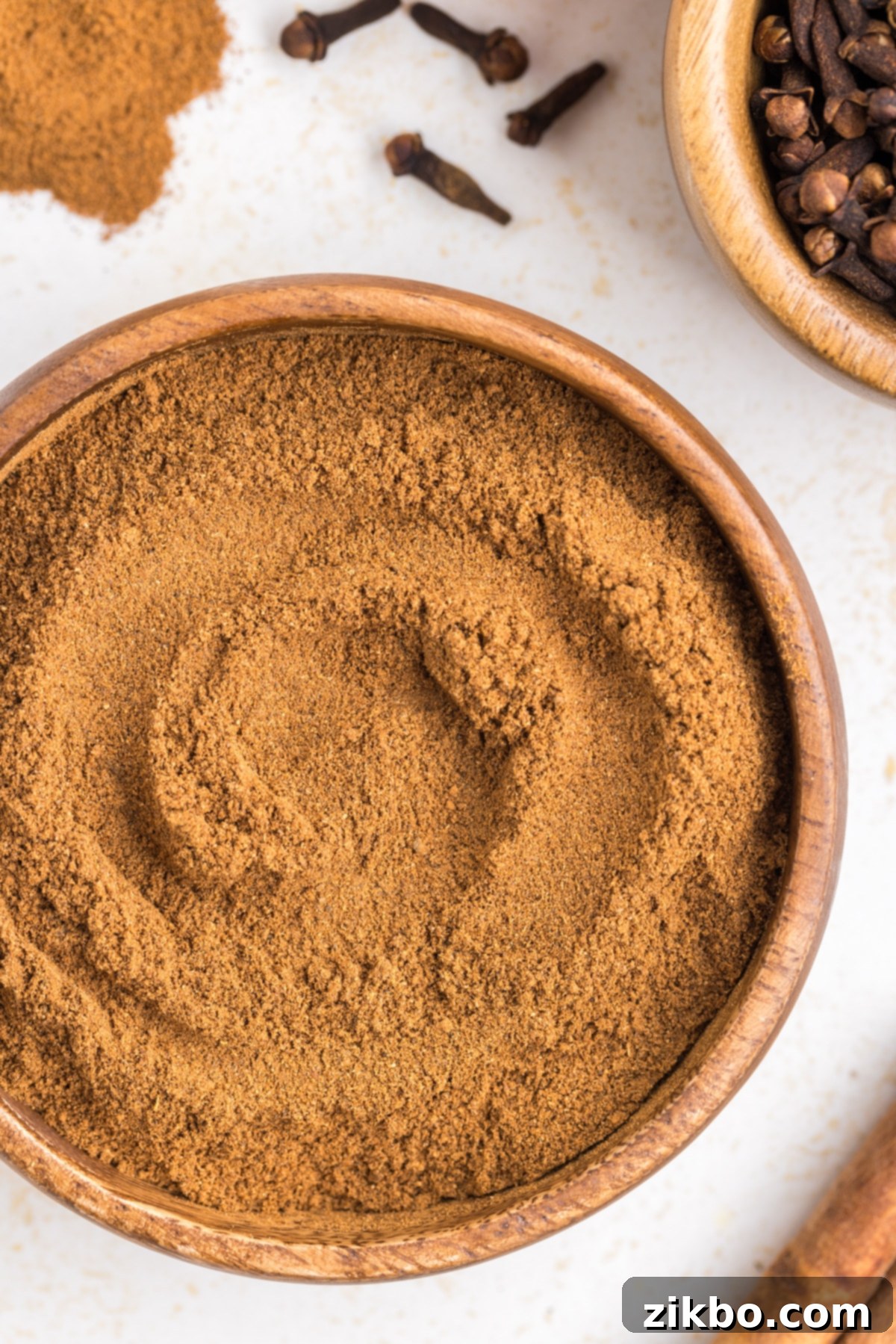 A small bowl of pumpkin spice blend, surrounded by whole cloves, star anise, and cinnamon sticks, highlighting its natural ingredients.