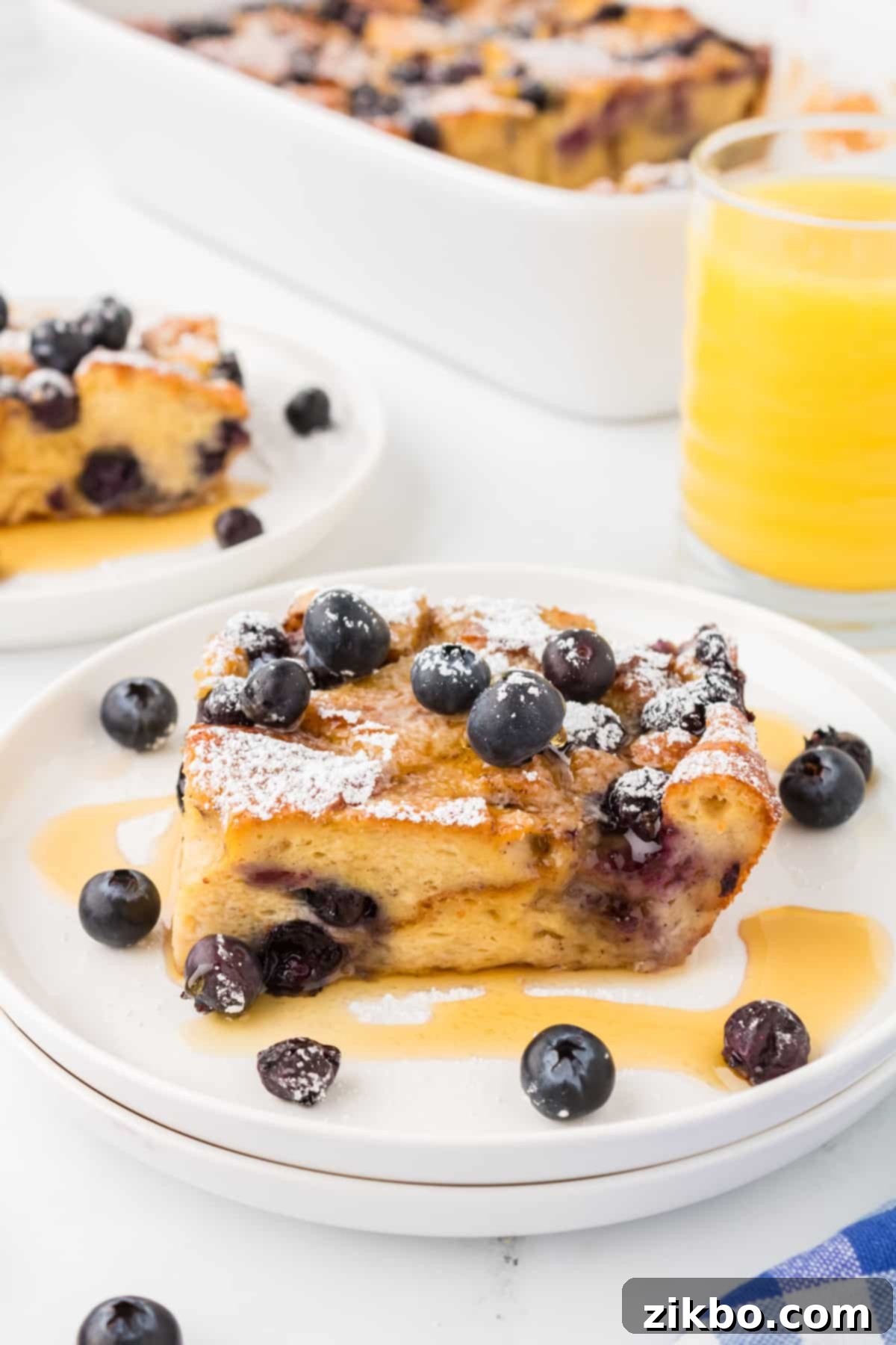 Overnight Brioche French Toast Bake 13 A square of baked brioche French toast garnished with blueberries and drizzled with maple syrup.