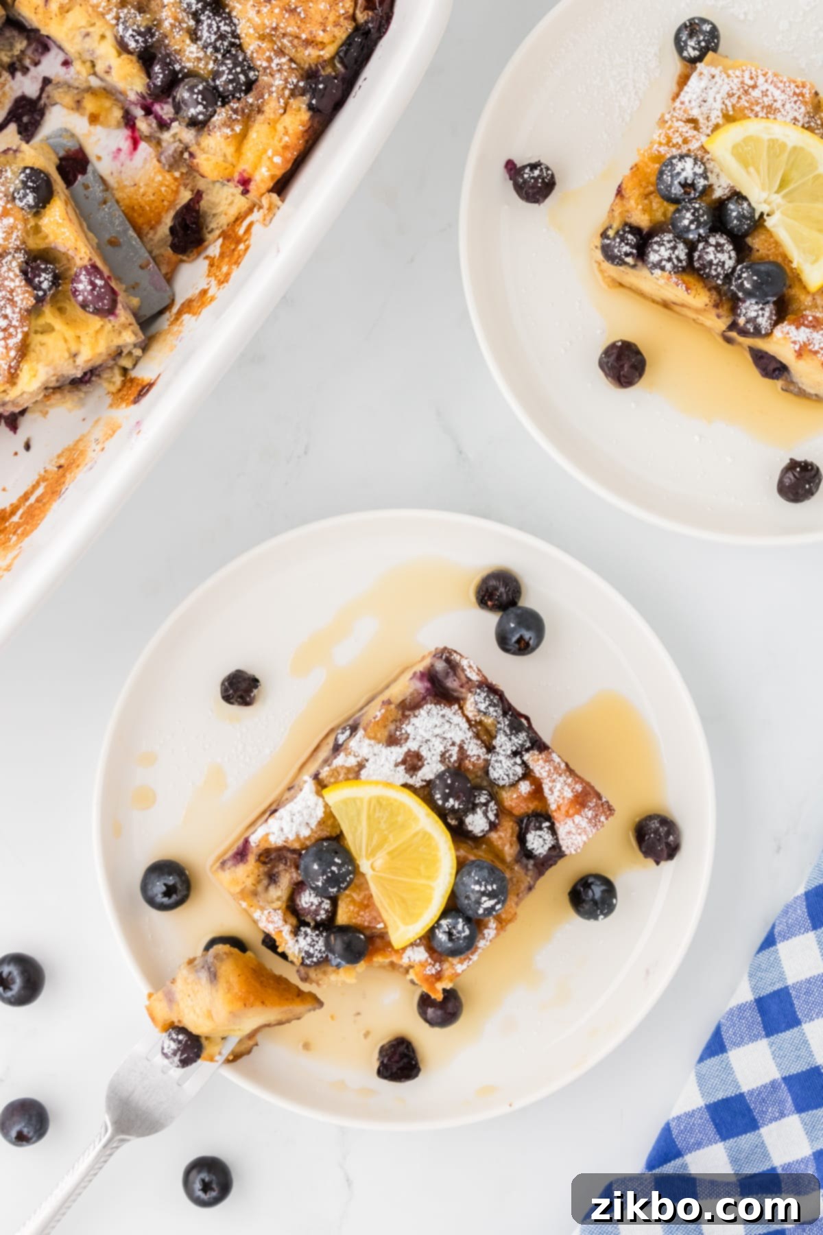 Overnight Brioche French Toast Bake 15 Baked brioche French toast casserole on a plate, garnished with lemon and blueberries and drizzled with maple syrup.