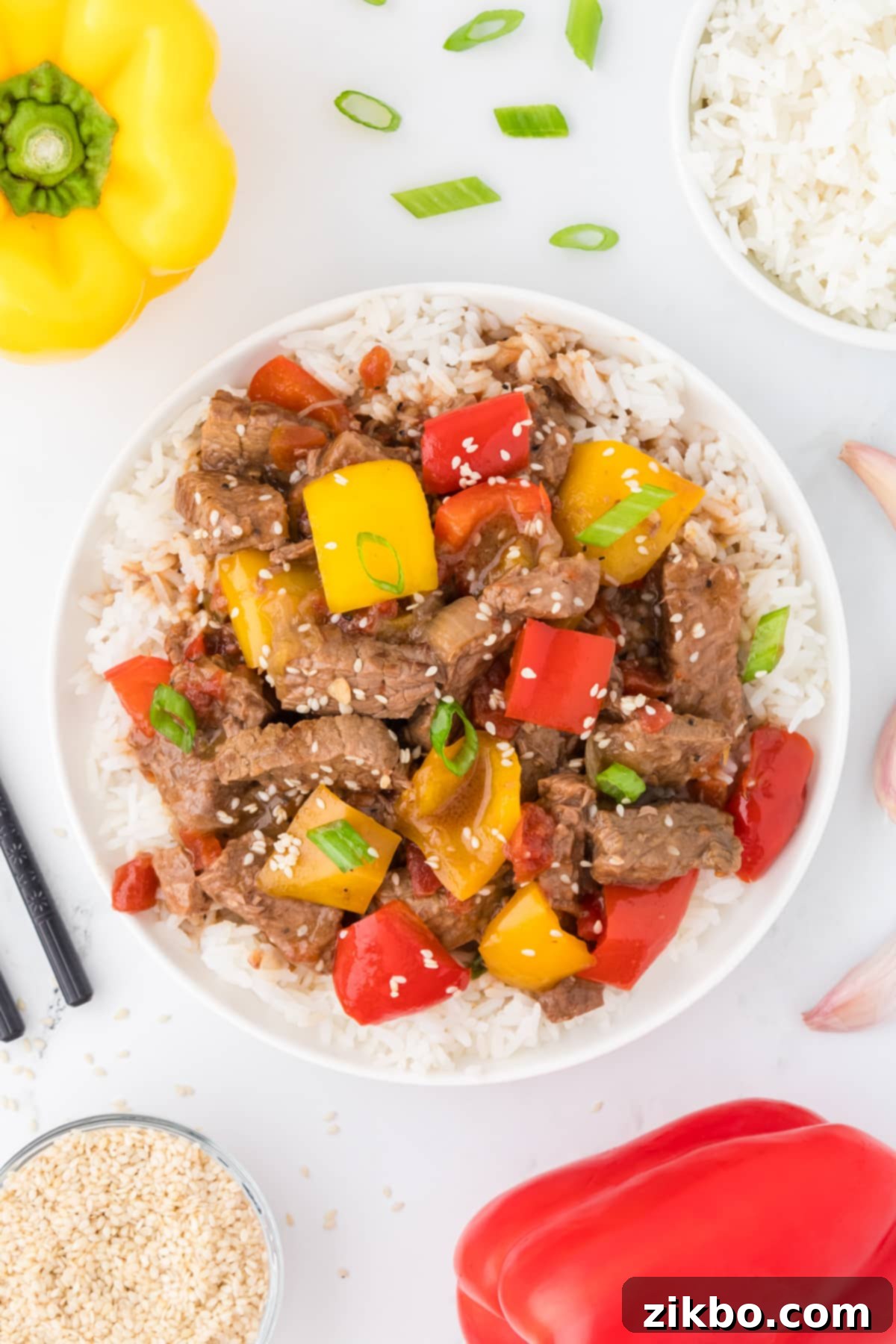 Slow Cooker Pepper Steak 2 An overhead view of a bowl of pepper steak served over rice, garnished with sesame seeds.