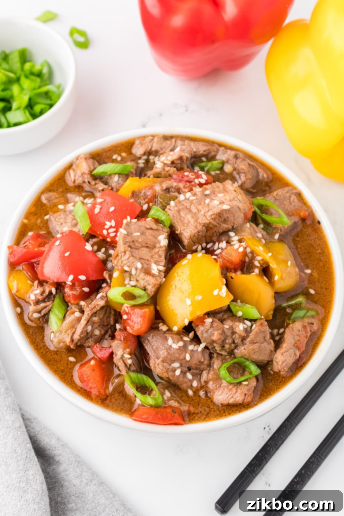 Slow Cooker Pepper Steak 14 A bowl of pepper steak stir fry with bell peppers, garnished with sesame seeds.