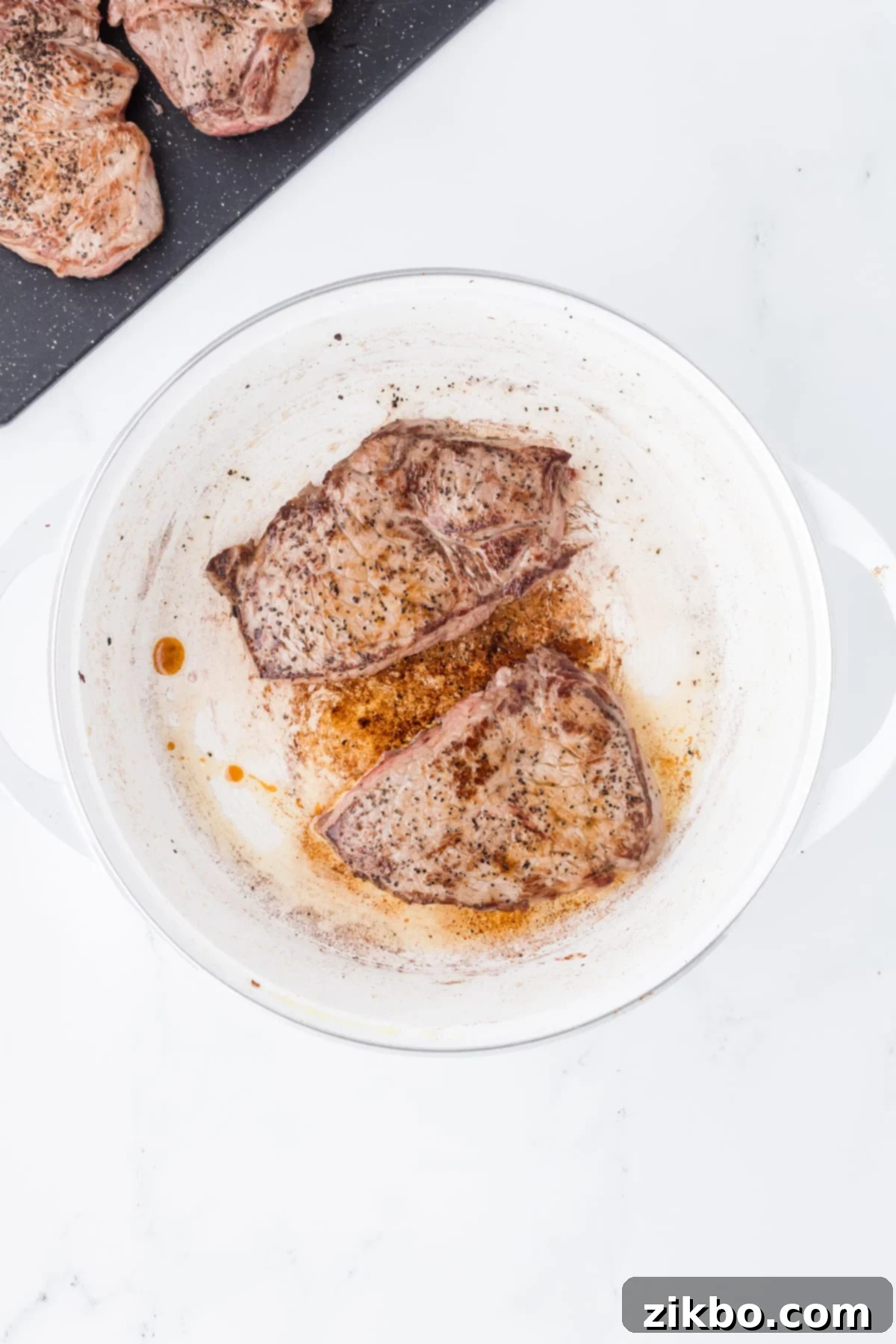 Slow Cooker Pepper Steak 5 Steaks that are browning in a Dutch Oven.