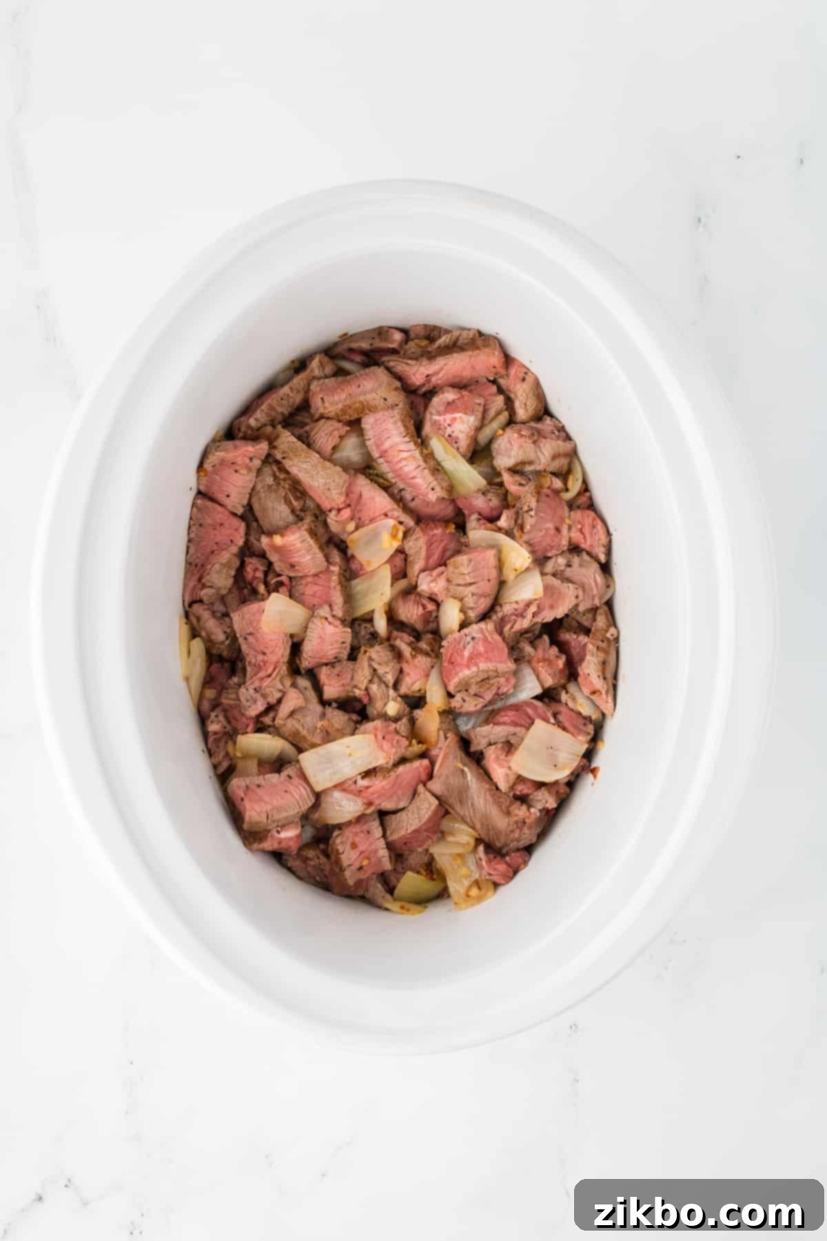Slow Cooker Pepper Steak 7 A slow cooker with beef and onions added.