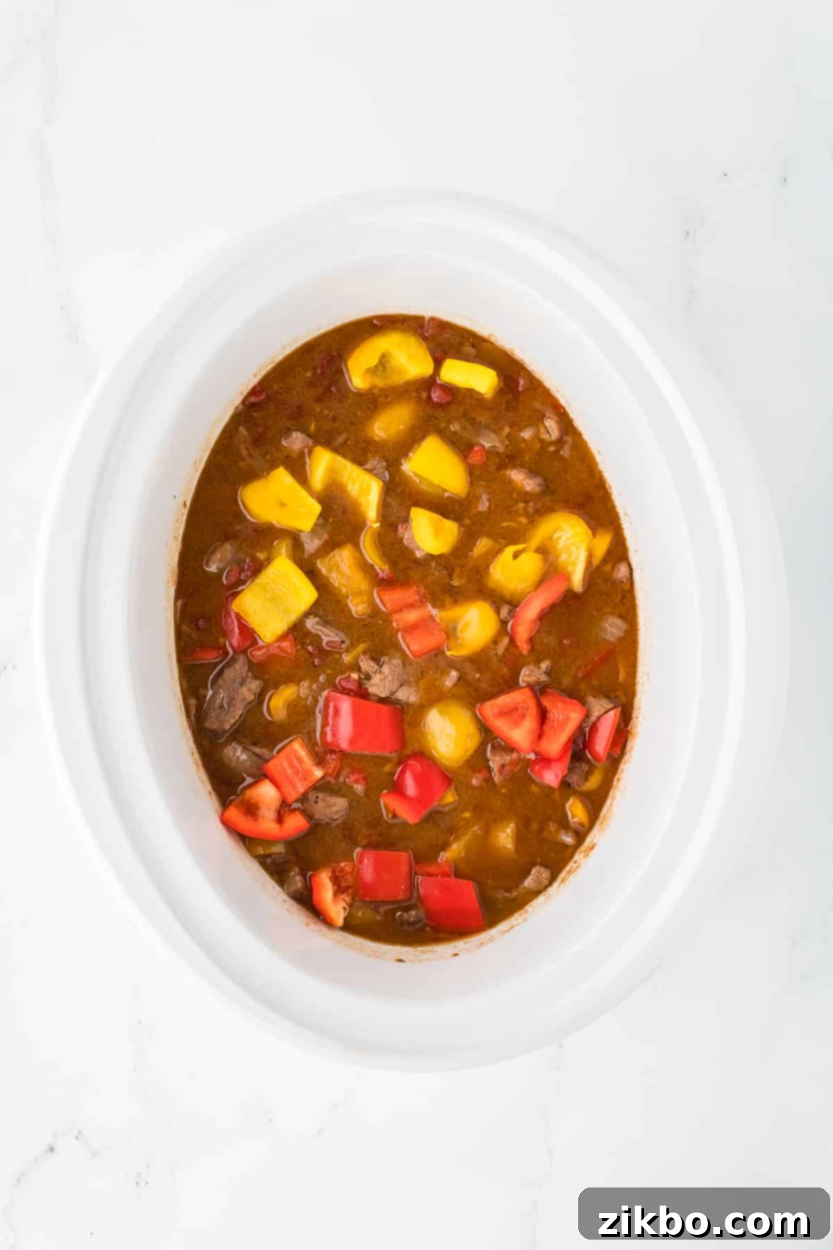 Slow Cooker Pepper Steak 10 A slow cooker filled with sauce, meat, and bell peppers.