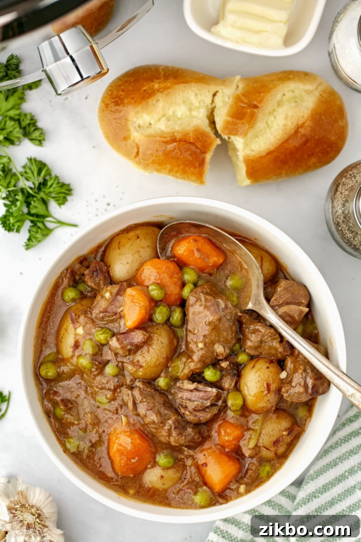 A bowl of beef stew with a small baguette on the side.