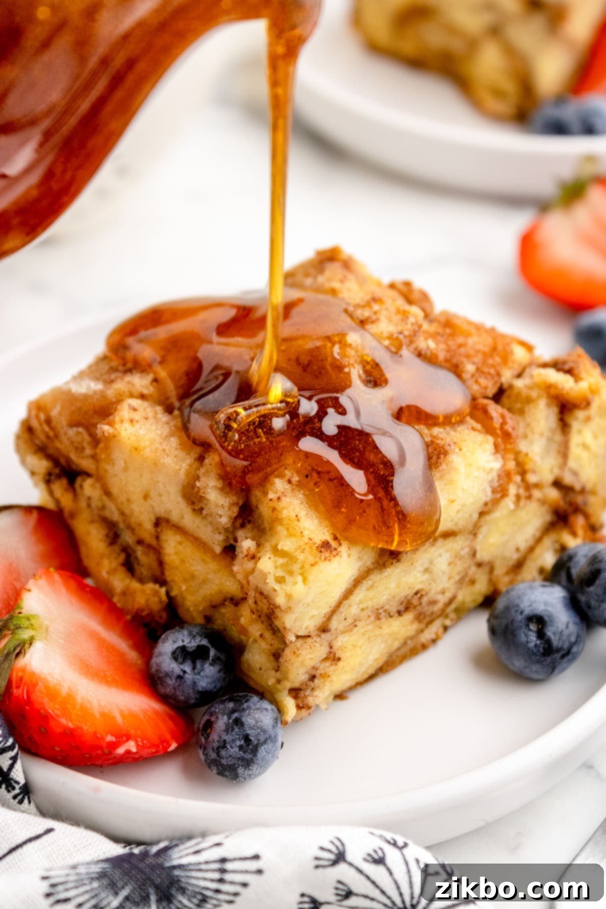 A square of golden French toast casserole drizzled generously with maple syrup, ready to be served.