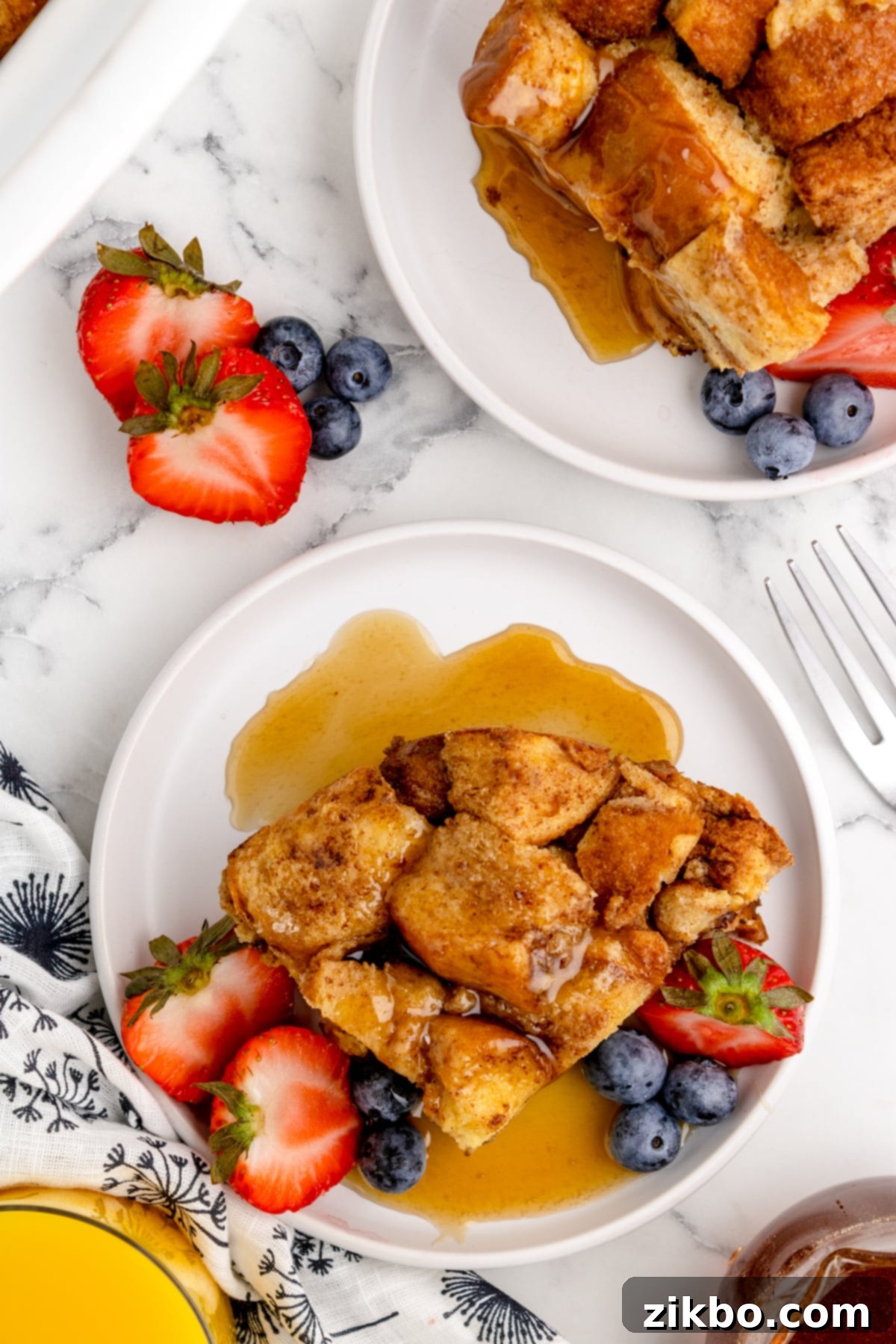 Two plates of French toast casserole, garnished with fresh berries and drizzled with sweet maple syrup, perfect for sharing.