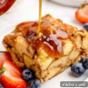 A square of French toast casserole drizzled with maple syrup and garnished with fresh berries, perfect for a special breakfast or brunch.