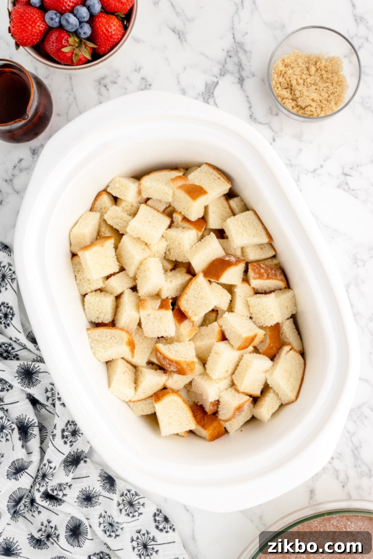 A slow cooker insert filled with dry bread cubes, ready for the custard mixture.