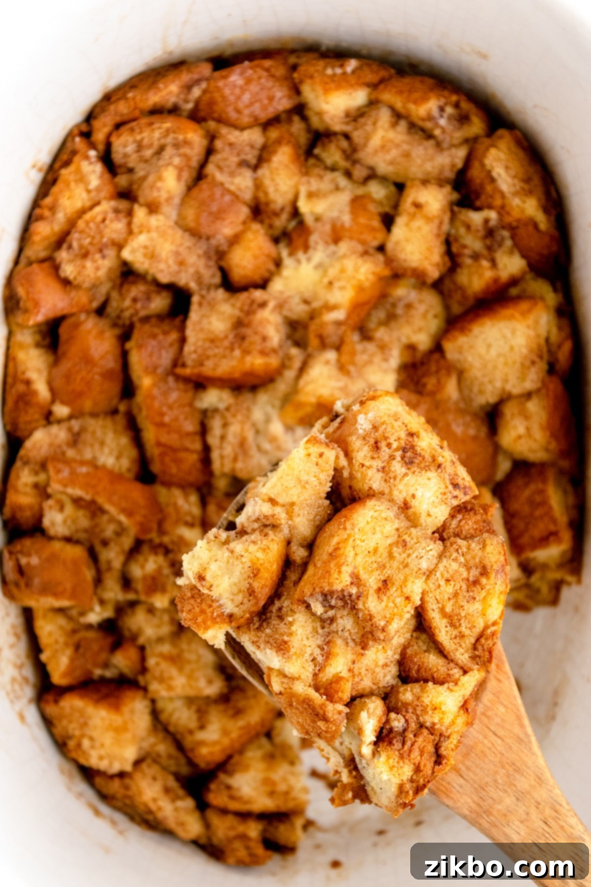 A spoon lifting a portion of French toast casserole from the slow cooker, ready to be served.