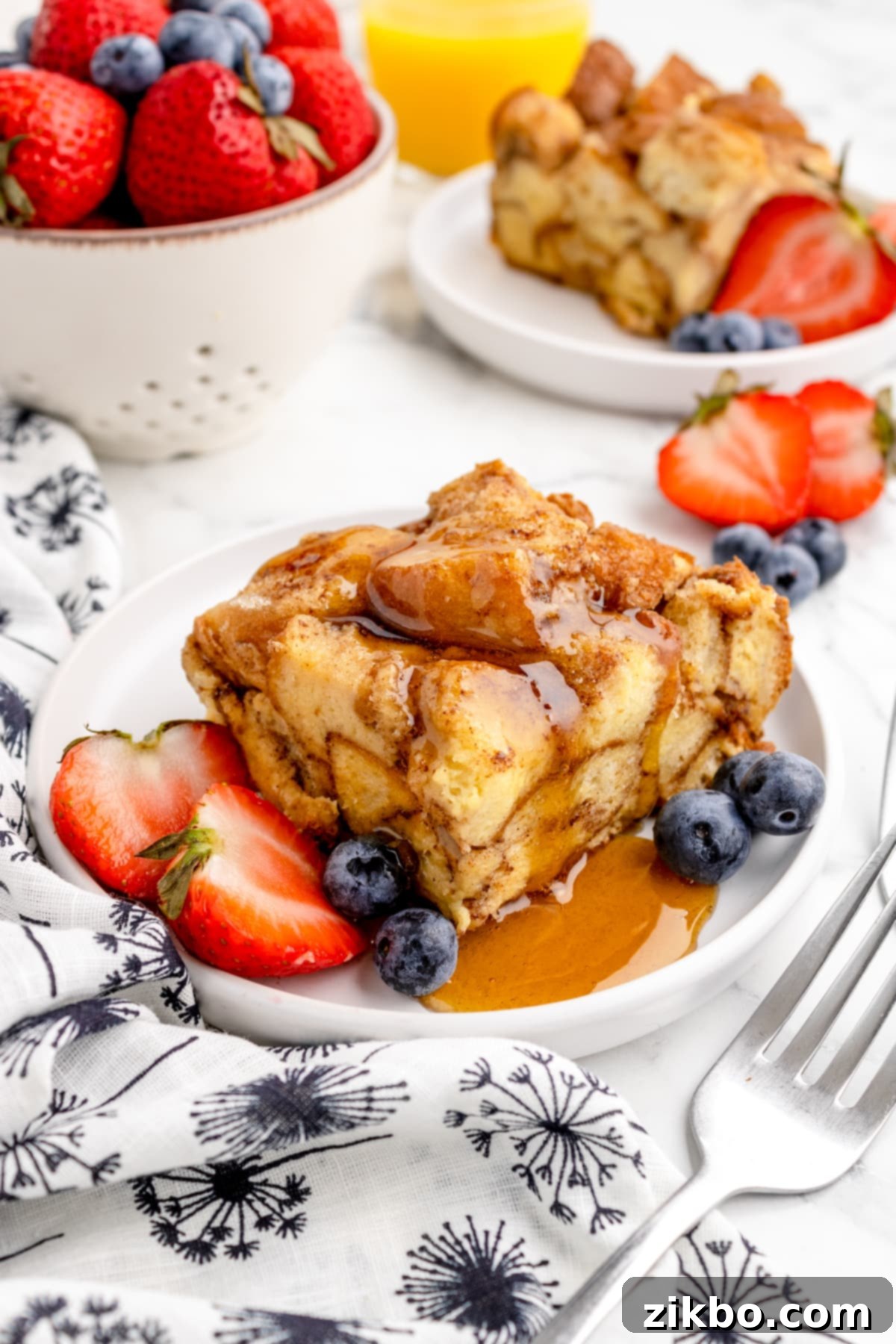 A square portion of Crock Pot French Toast Casserole garnished with fresh berries and drizzled with maple syrup.