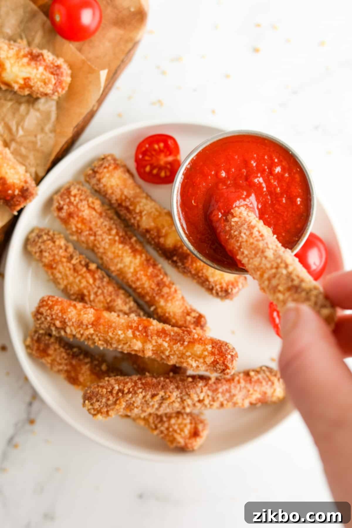 A plate with halloumi fries, and dipping one into a pizza sauce. This highlights the crispy texture and delicious appeal of air-fried halloumi cheese sticks.