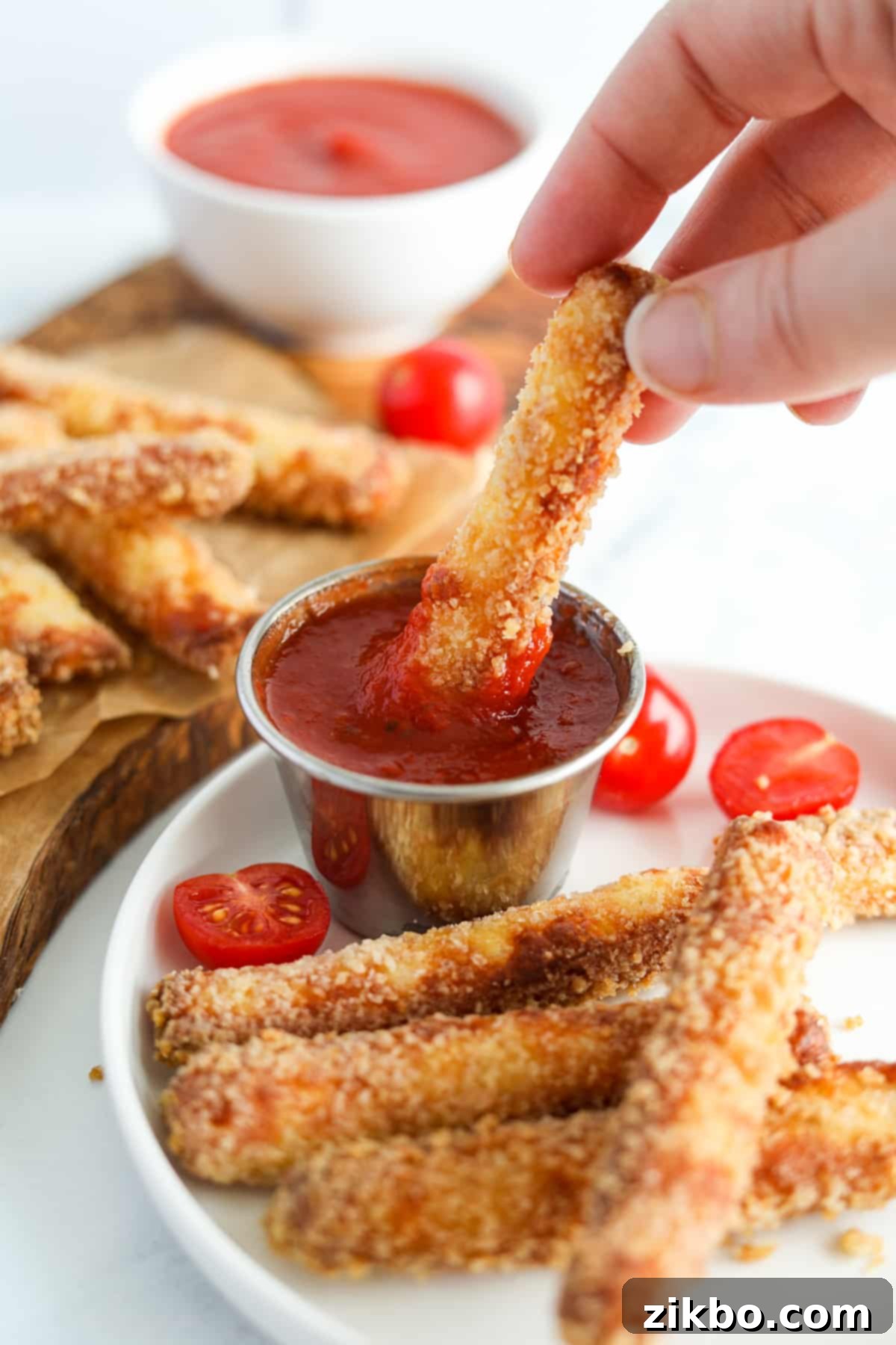 A close-up of a hand dipping a crispy halloumi fry into a bowl of vibrant marinara sauce, showcasing its delicious appeal.