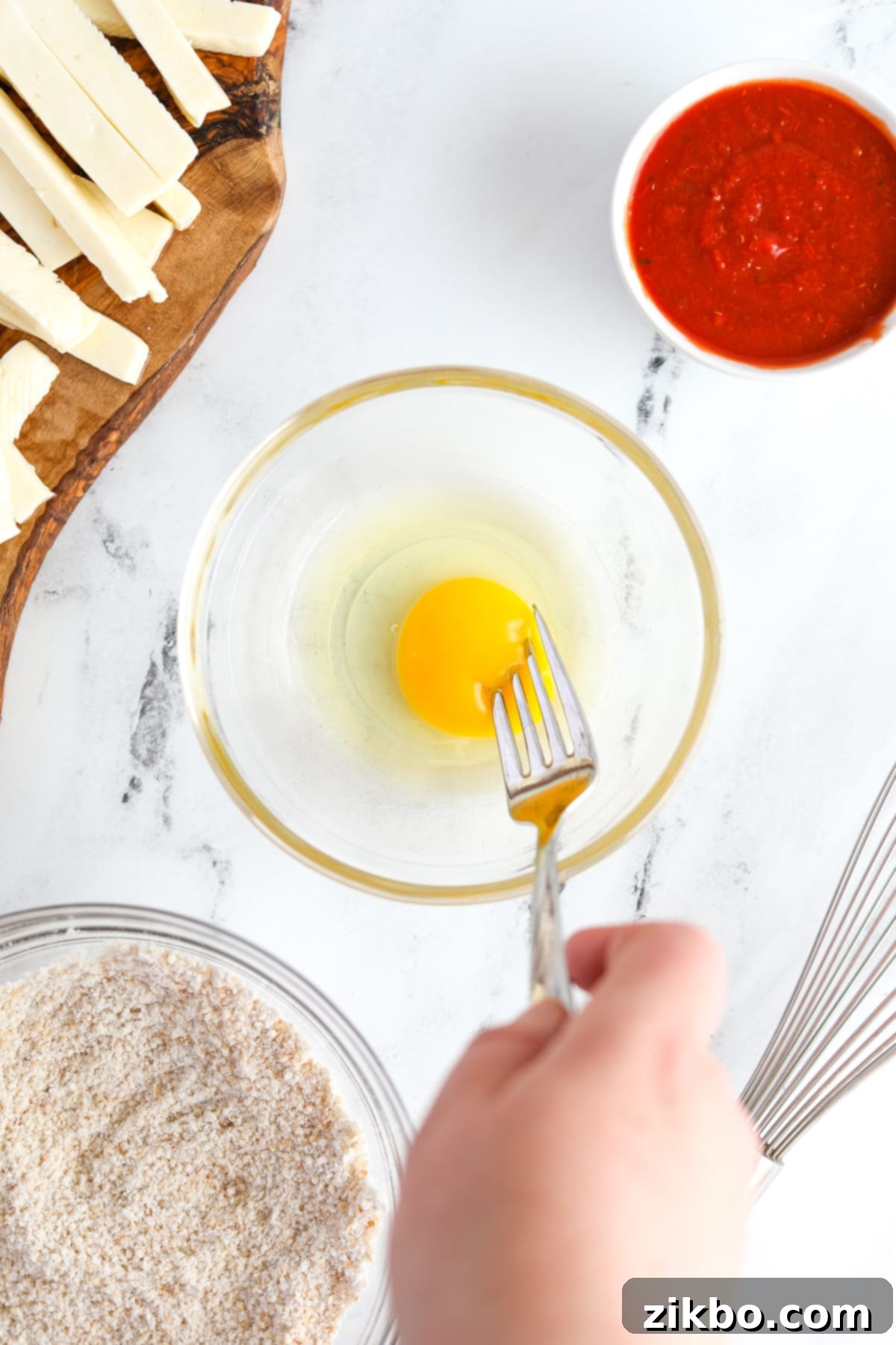 Whisking an egg in a small, shallow bowl to prepare the wet coating for the halloumi fries.