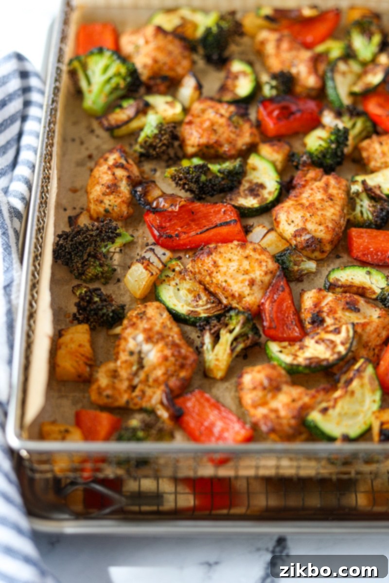 A parchment lined air fryer tray filled with veggies and chicken pieces.
