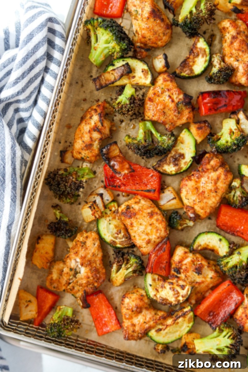 An air fryer tray lined in parchment and filled with cooked chicken pieces and vegetables.