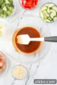 A bowl with a silicone spatula stirring seasonings and oil together.