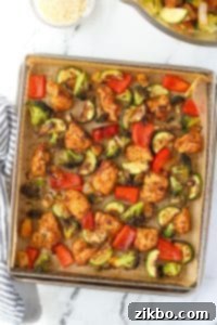An air fryer tray with chicken and vegetables spread in an even layer.