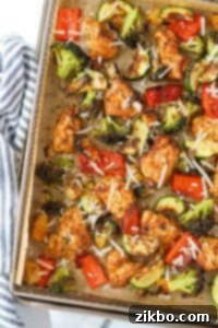 An air fryer tray filled with a medley of chicken and vegetables, sprinkled with parmesan cheese.