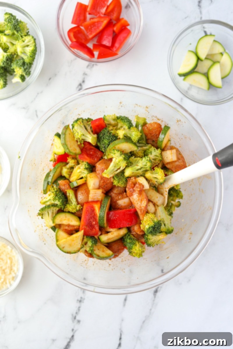 A bowl of vegetables and chicken tossed with seasoning and oil.