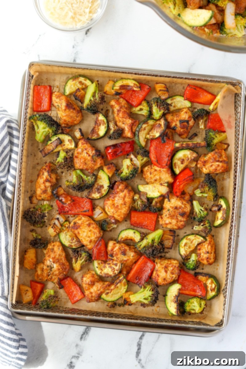 An air fryer tray with chicken and vegetables spread in an even layer.