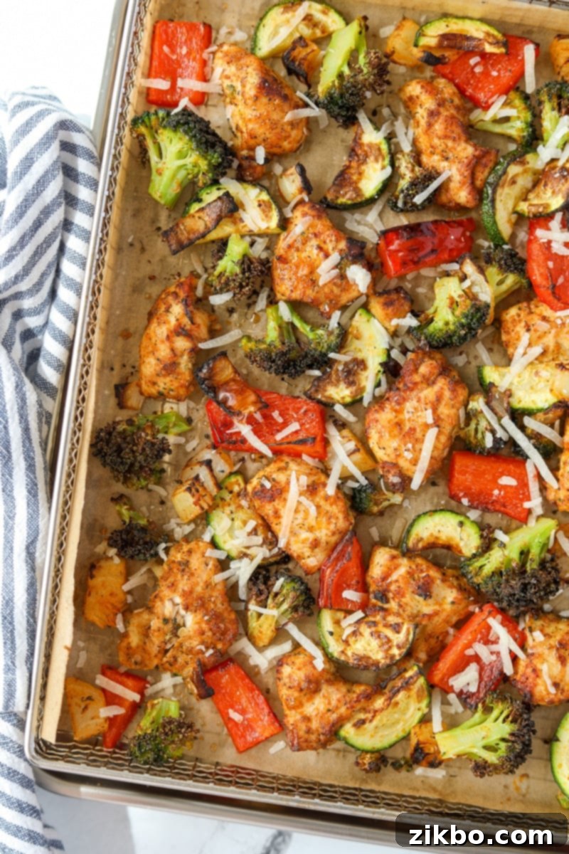 An air fryer tray filled with a medley of chicken and vegetables, sprinkled with parmesan cheese.