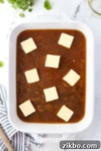 A baking dish with butter pats on top of a liquid and rice mixture.