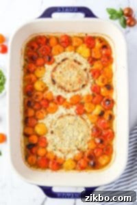 A baking dish with roasted cherry tomatoes and blistered cheese after baking.