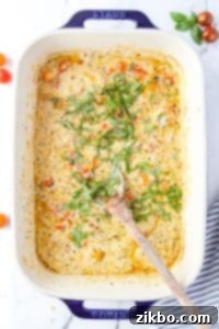 A baking dish filled with a creamy sauce and fresh chopped basil being stirred in.