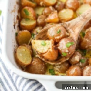 A wooden spoon scooping cooked baby potatoes from a baking dish.