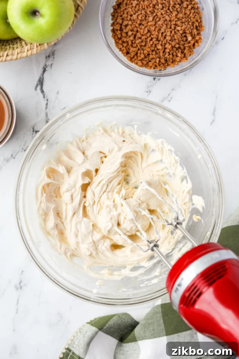 Creamy Caramel Apple Delight 5 An electric hand mixer actively beating the ingredients in a bowl, creating a smooth and creamy cream cheese mixture.