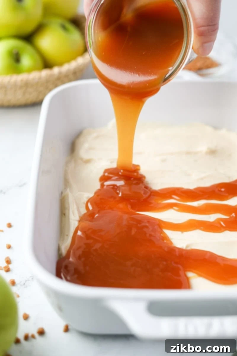 Creamy Caramel Apple Delight 7 Thick, golden caramel sauce being artfully drizzled over the smooth, white cream cheese layer in a baking dish, creating the next delicious tier.
