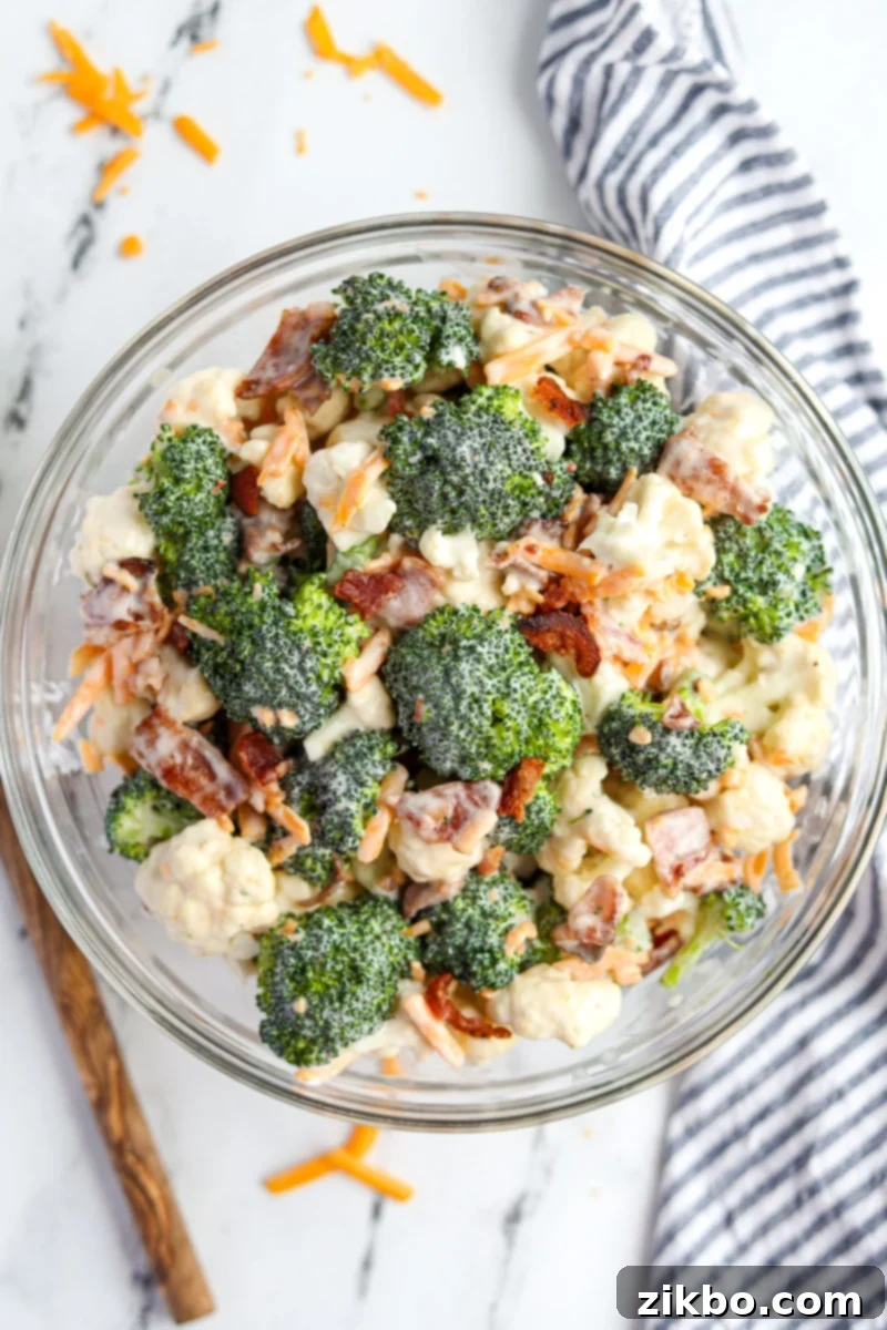 A vibrant bowl of creamy Amish broccoli salad featuring broccoli florets, cauliflower, crumbled bacon, and shredded cheddar cheese.