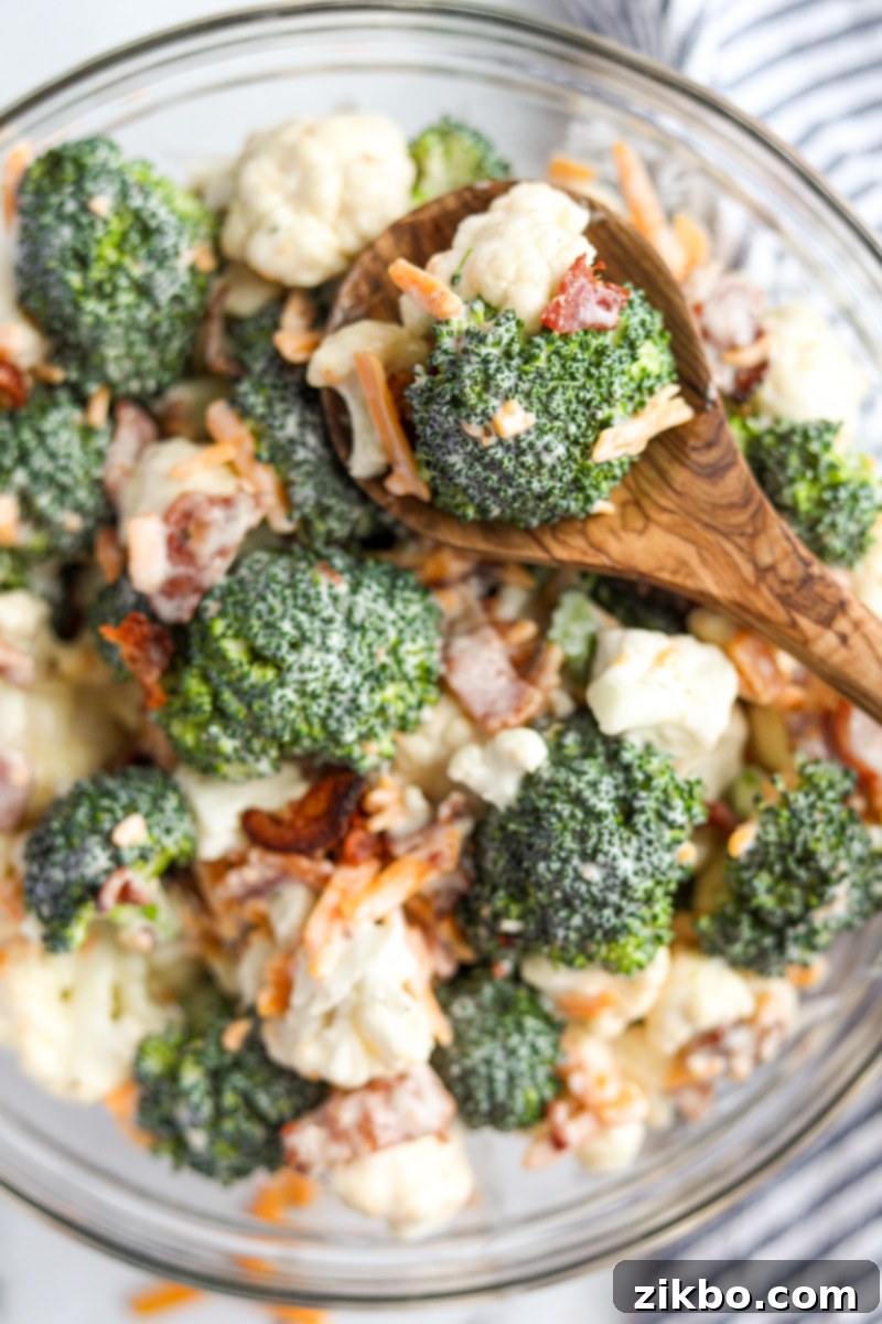 A large bowl of creamy Amish broccoli salad, with a wooden serving spoon scooping out a portion, highlighting the rich texture and colorful ingredients.