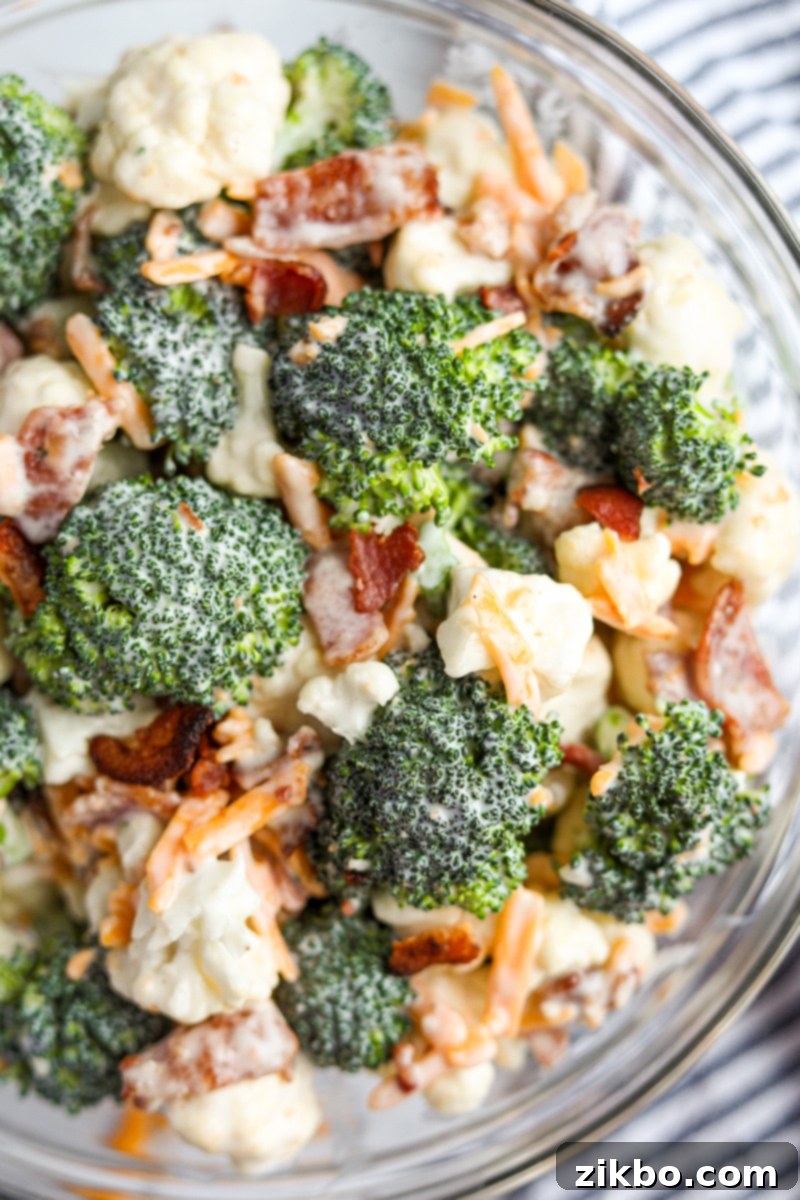 A close-up, appetizing view of a bowl of creamy Amish broccoli salad, showcasing the texture of the broccoli and cauliflower florets, the melted cheese, and the crispy bacon pieces.