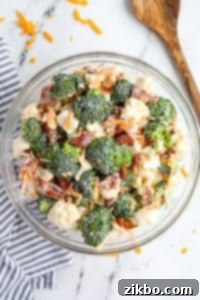 A bowl filled with broccoli and cauliflower salad, topped with cheese and bacon.