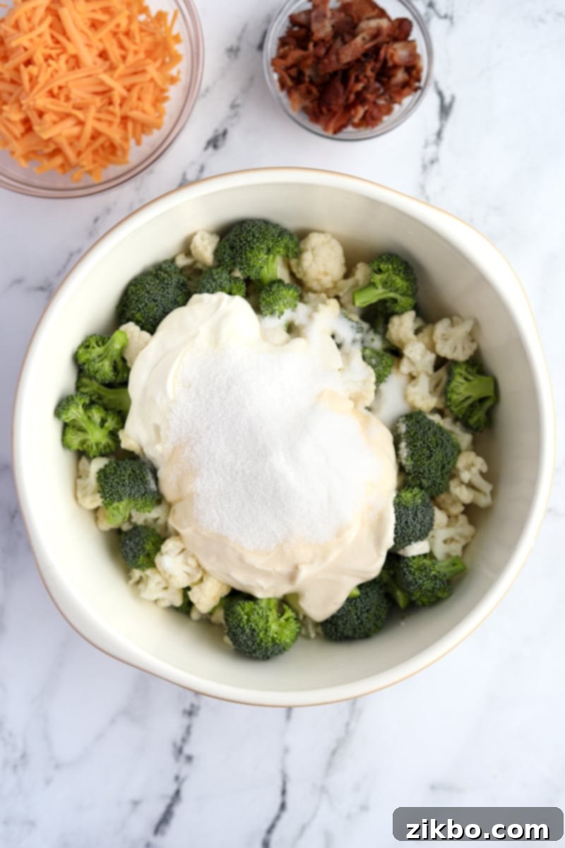 A generous dollop of creamy white dressing placed on top of a pile of raw cauliflower and broccoli florets in a large bowl.