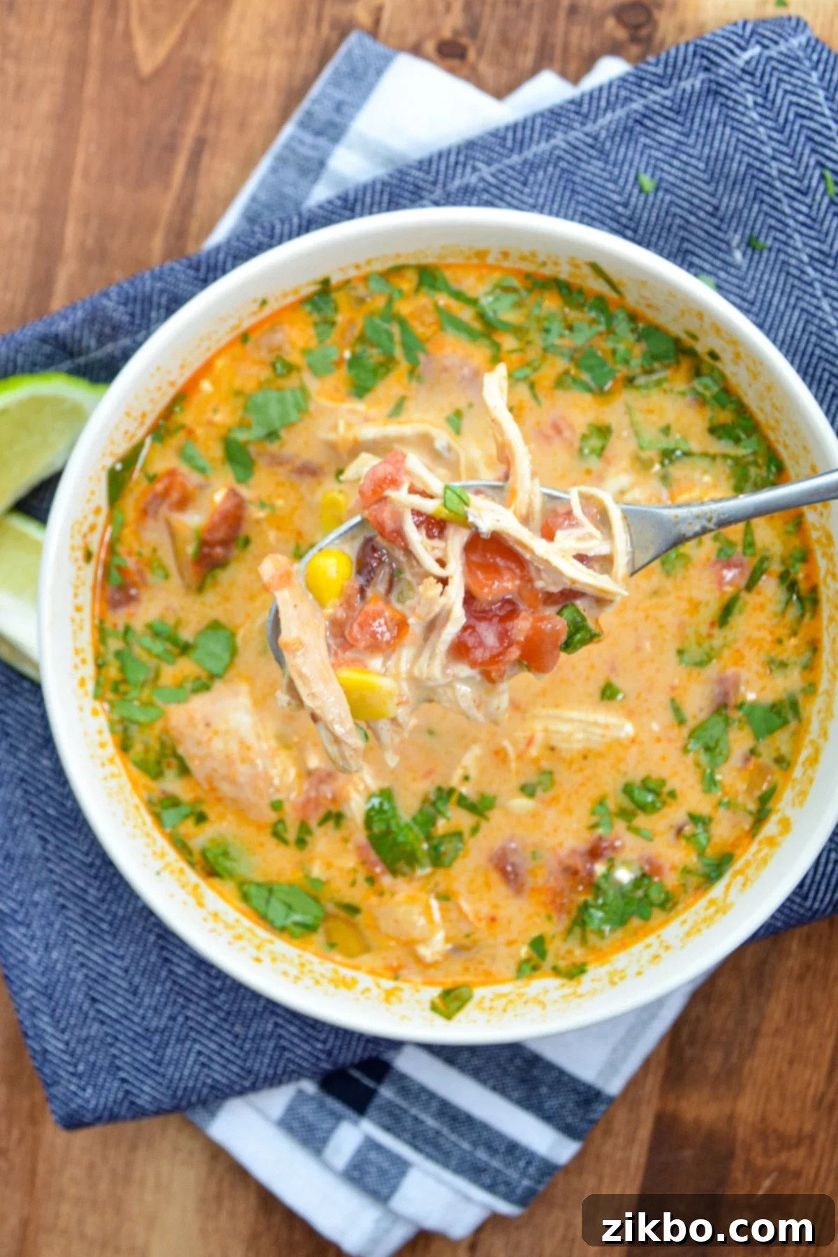 A vibrant bowl of creamy chicken tortilla soup, garnished with fresh cilantro and a lime wedge, resting on rustic blue napkins.
