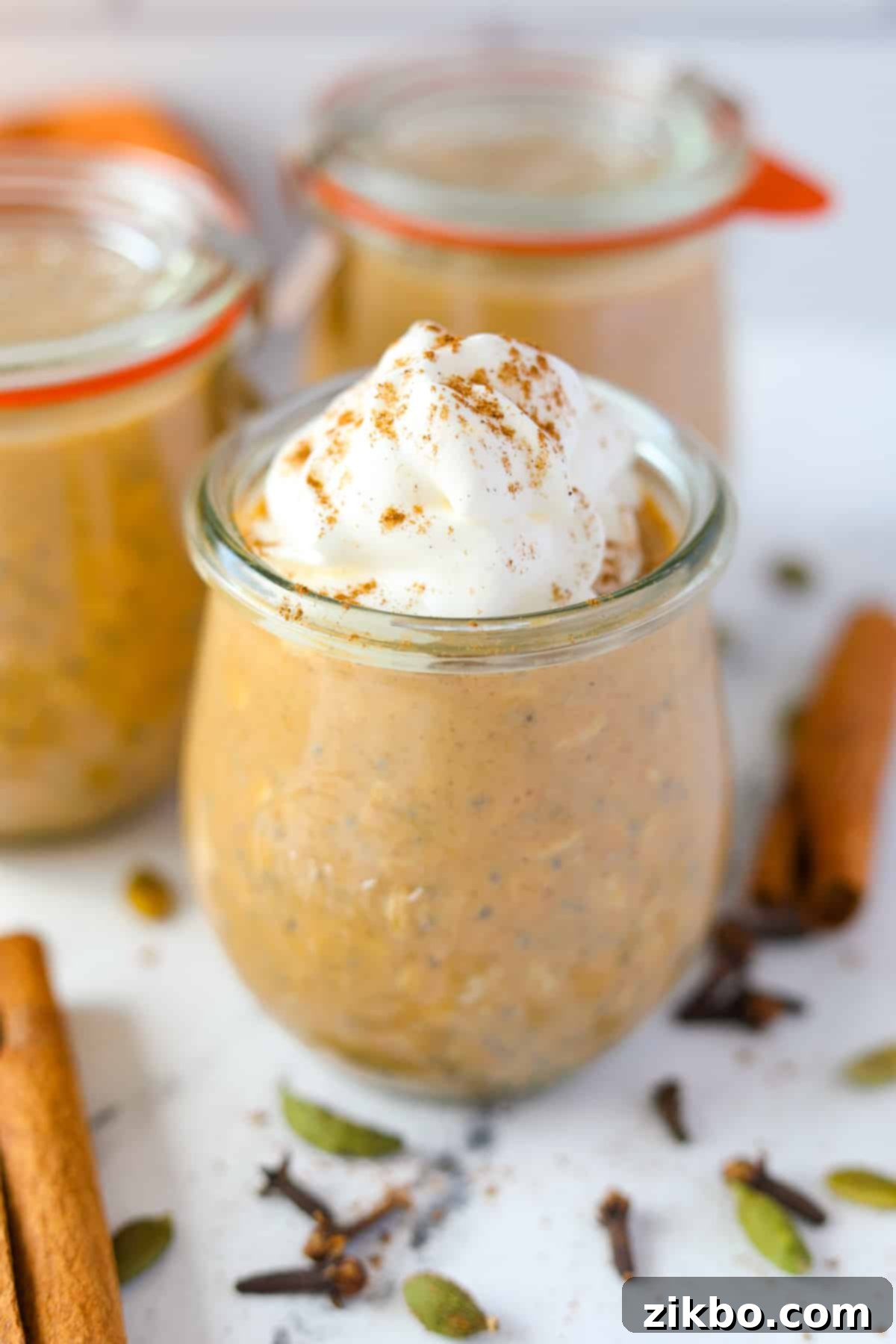 A jar of overnight oats, garnished with whipped cream and a pinch of pumpkin spice on top.