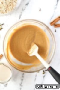 A silicone spatula stirring a pumpkin colored liquid.
