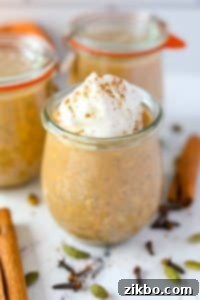 A jar of overnight oats, garnished with whipped cream and a pinch of pumpkin spice on top.