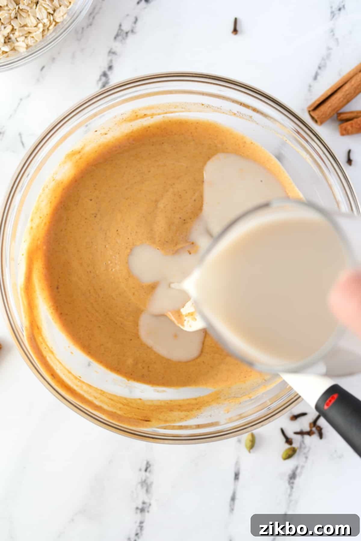Adding cashew milk to a bowl full of pumpkin colored liquid.