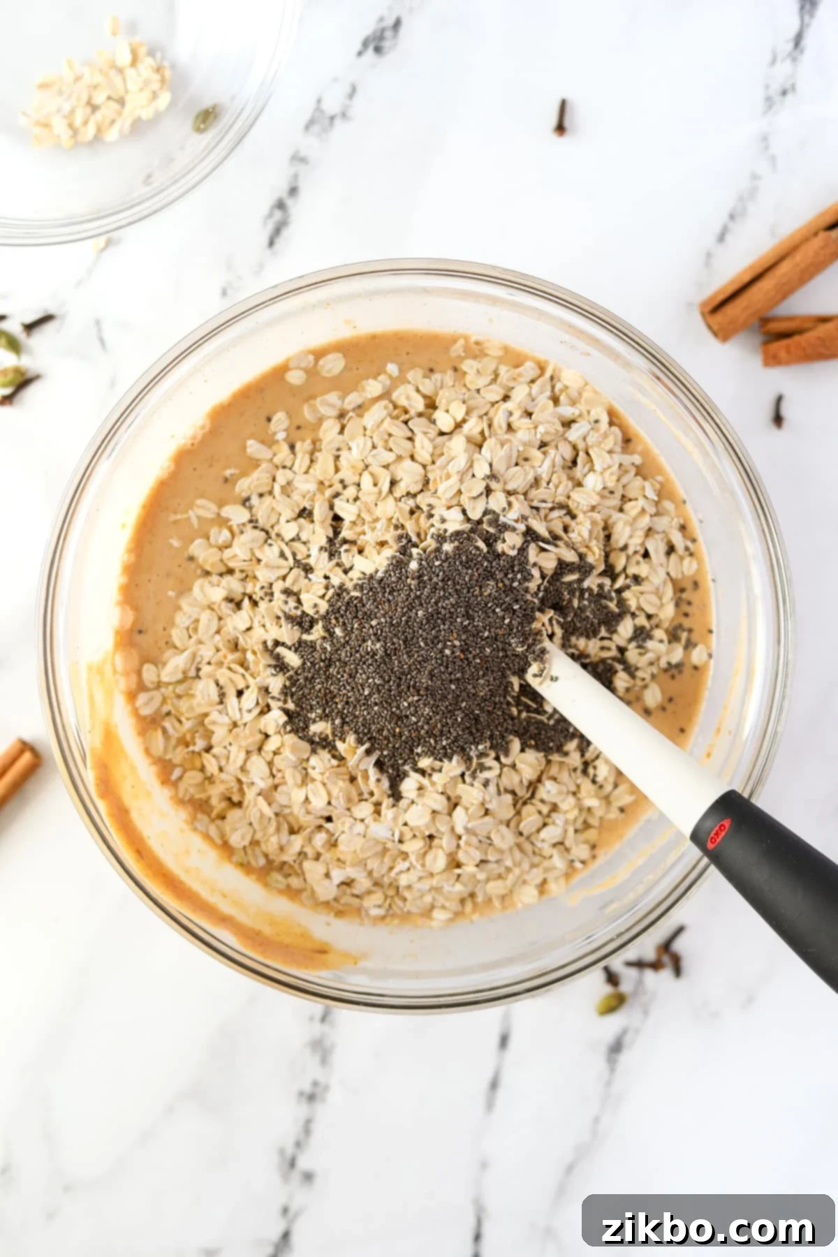 Adding oats and chia seeds to a bowl of pumpkin colored liquid.