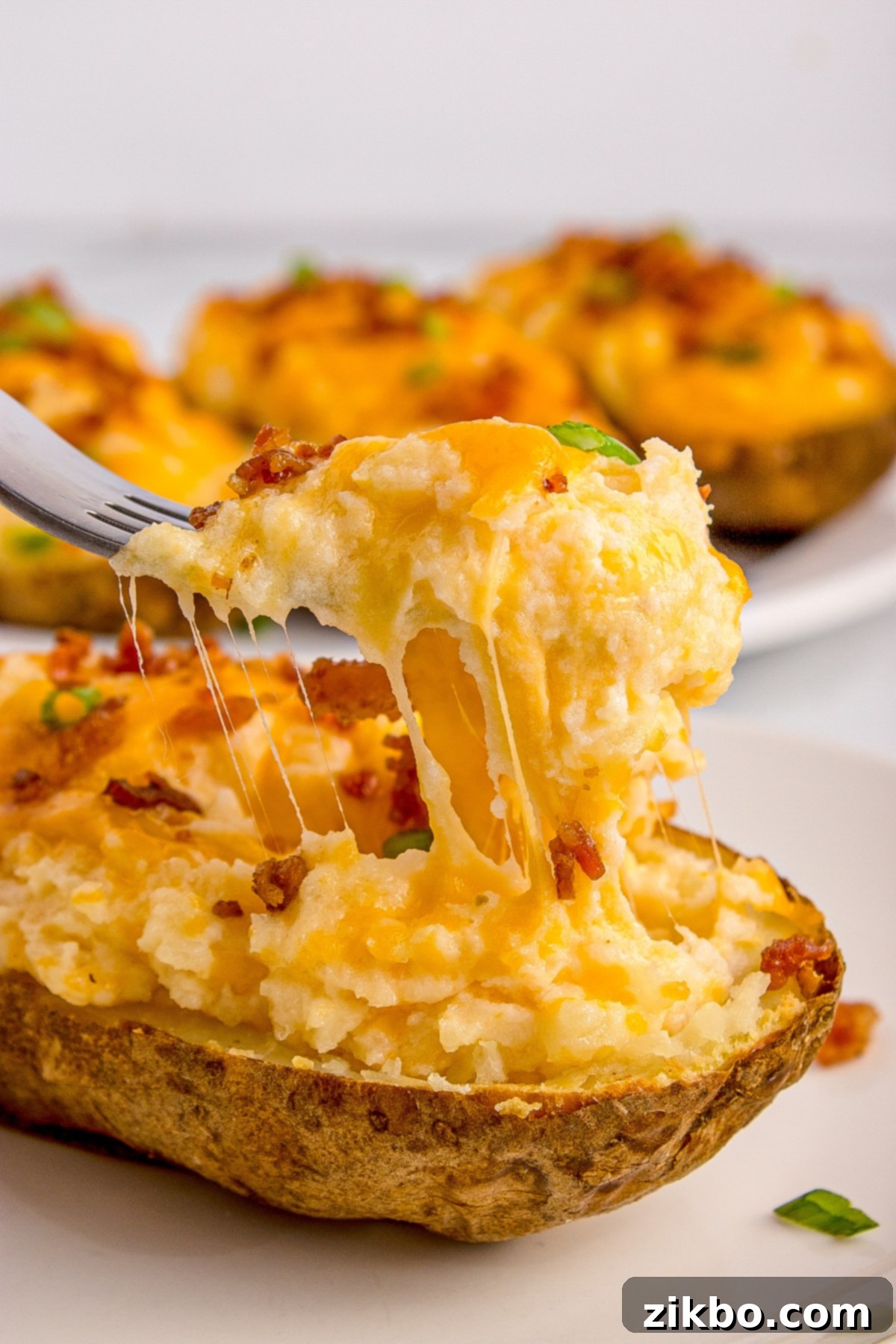 Perfectly Crispy Air Fryer Twice Baked Potatoes 13 A fork pulling a string of melted cheese from a generously stuffed, air-fried twice baked potato, highlighting its creamy texture.