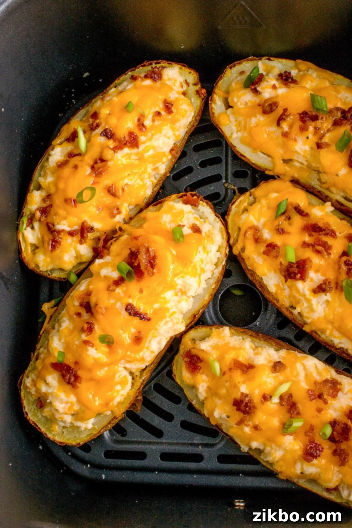 Perfectly Crispy Air Fryer Twice Baked Potatoes 14 An air fryer basket filled with five beautifully stuffed potato halves, each generously topped with melted cheese and crispy bacon, ready to be served.
