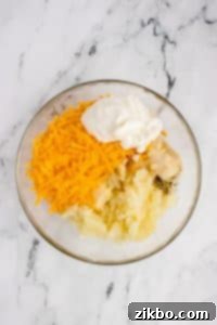 A bowl with mashed potato, cheese, sour cream, and spices.